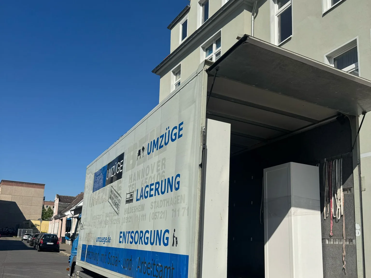 Umzugswagen mit ausgefahrener Ladebordwand vor einem Wohnhaus, im Laderaum steht ein Kühlschrank